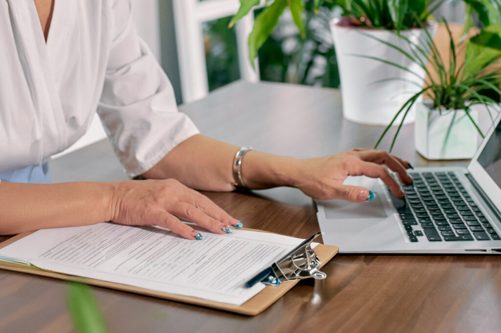 Person reviewing compliance documents beside a laptop