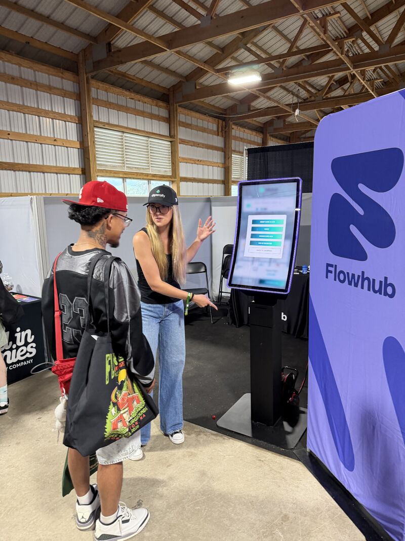 A Dispensify team member demonstrating a curved kiosk beside the Flowhub display at Flower Expo Northampton